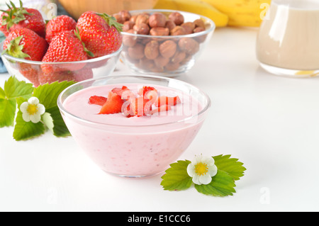 Delizioso yogurt alla fragola sul tavolo bianco. Home fatta di yogurt con le fragole in un recipiente di vetro e fragole Fiori. Foto Stock