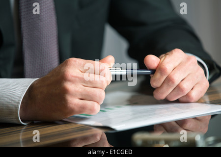 Uomo con le mani in mano in possesso di una penna nera in entrambe le braccia in un gesto di pensiero durante una riunione o negoziazione Foto Stock