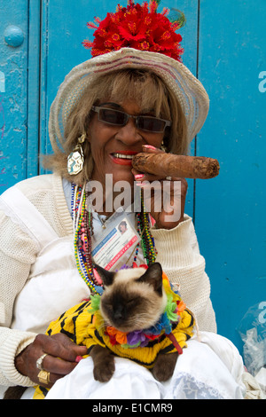 Donna cubana di fumare un sigaro, in posa con il suo gatto e sorridente a La Habana Vieja, Old Havana, Cuba Foto Stock