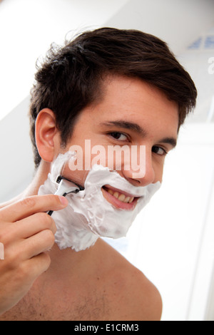 Giovane uomo la rasatura con il rasoio e crema di rasatura nella stanza da bagno Foto Stock