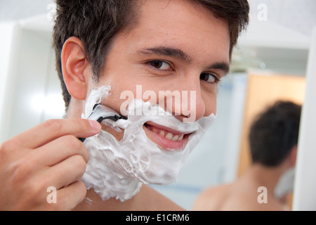 Giovane uomo la rasatura con il rasoio e crema di rasatura nella stanza da bagno Foto Stock