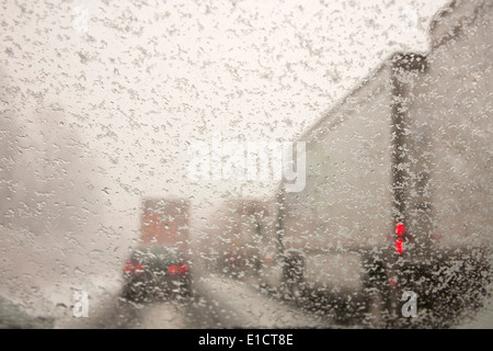 Automobili e camion guida su neve imballata strade presa attraverso un parabrezza coperta con i fiocchi di neve. Foto Stock