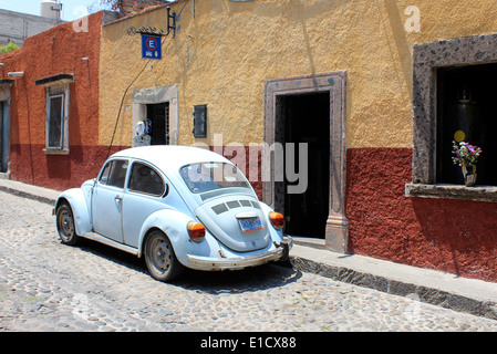 Auto blu chiaro VW Beetle o vocho messicano fuori tipiche case coloniali colorate lungo la strada acciottolata a San Miguel de Allende, Guanajuato, Messico Foto Stock