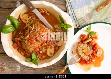 Tagliate a fette polpettone saporito con funghi e verdure servita in una casseruola con il coltello e la forchetta su una tavola in legno rustico Foto Stock