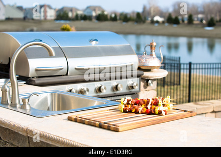 Kebab giacente su una tavola di legno sul contatore di un dehor estivo cucina accanto al barbecue a gas pronto per essere cotto per una salute Foto Stock