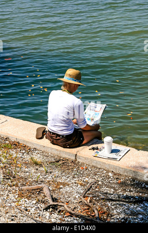 Una donna si siede sul lungomare e legge la sua carta, beve il suo caffè e gode di un momento solitario in Florida Foto Stock