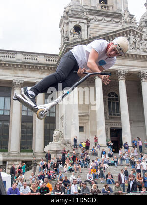 Un giovane pilota di scooter esegue un' antenna stunt davanti a folle si radunarono in Portsmouth Guildhall passi, durante il Portsmouth street Games 2014 Foto Stock