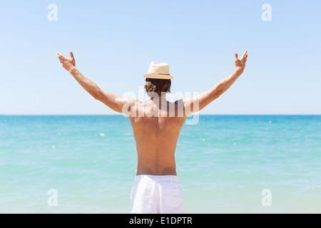 Uomo sulla spiaggia tenere mani le braccia in alto, vista posteriore Foto Stock