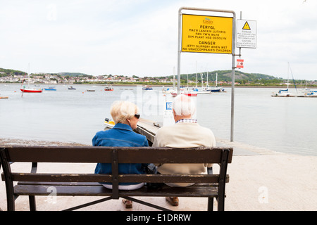 Senior l uomo e la donna seduta sulla panca in legno, godendo della vista sul mare, accanto al molo, in Conway il Galles del Nord Foto Stock