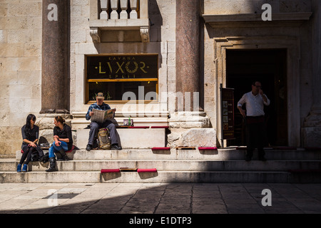 Due donne parlare mentre un uomo legge un giornale in peristil nel palazzo di Diocleziano, Split, Croazia. un cameriere si affaccia su Foto Stock