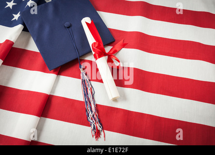 Tappo di graduazione con fiocco e nastro rosso avvolto Diploma in appoggio sulla bandiera americana. Foto Stock