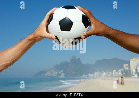 Il brasiliano interracial mani tenendo il calcio al di sopra di due fratelli di montagna la spiaggia di Ipanema di Rio de Janeiro in Brasile Foto Stock