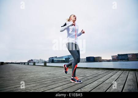 Basso angolo vista di atleta femminile che corre lungo il lungomare. Giovane donna di jogging sul lungomare dal fiume. Foto Stock