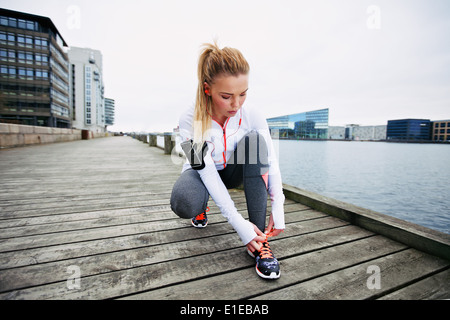 Giovane donna la sua legatura lacci delle scarpe prima di correre lungo il lungomare. Femminile preparazione foe sprint. Montare atleta femminile Foto Stock