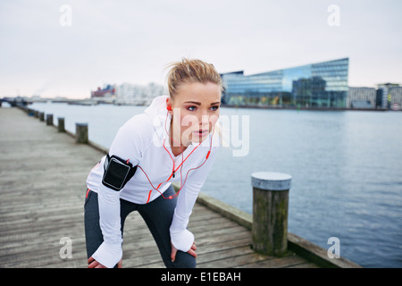 Giovani femmine runner fermandosi per un riposo mentre fuori su una corsa lungo il fiume. Donna Fitness prendendo una pausa dalla sessione di formazione. Foto Stock