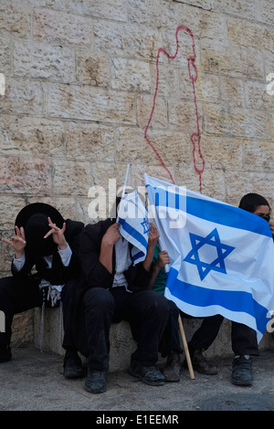 Gli ebrei ortodossi di nascondersi dietro la bandiera israeliana con graffiti nella parete raffiguranti lo stato di Israele nella città vecchia di Gerusalemme Foto Stock