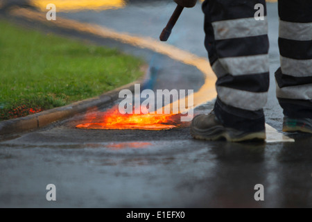 Un lavoratore utilizzando una lancia di gas brucia esistenti linee gialla prima di loro rinfrescante Foto Stock