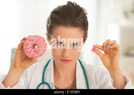 Grave medico donna che mostra a ciambella e pillola Foto Stock