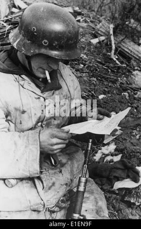 Un soldato dell'esercito tedesco legge una lettera in un rifugio lungo il fronte orientale nel maggio 1943. Il testo originale del rapporto nazista recita: 'Mentre le truppe di ricognizione sono fuori con il nemico, è arrivato il posto da tempo atteso sul campo. Tutte le emozioni e le tensioni sono dimenticate. Non c'è nemmeno abbastanza tempo per posare il fucile o il casco in acciaio: Le lettere da casa sono molto più importanti." Fotoarchiv für Zeitgeschichtee - NESSUN SERVIZIO DI CABLAGGIO Foto Stock