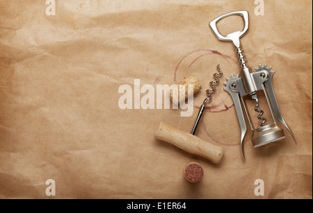 Sughero e cavatappi con un bicchiere di vino rosso le macchie sulla carta marrone sfondo con spazio di copia Foto Stock