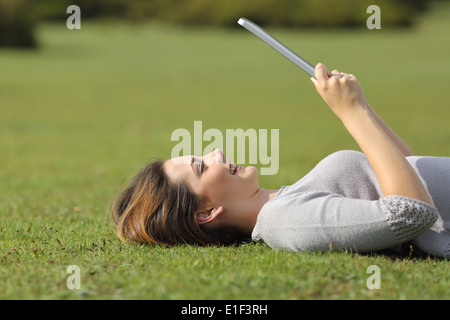 Profilo di una donna felice di lettura di un lettore di tablet sul prato di un parco Foto Stock