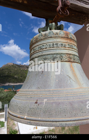 Villaggio di Assos, Cefalonia. Vista ravvicinata di una campana da Agios Georgios chiesa con Assos castello in background. Foto Stock