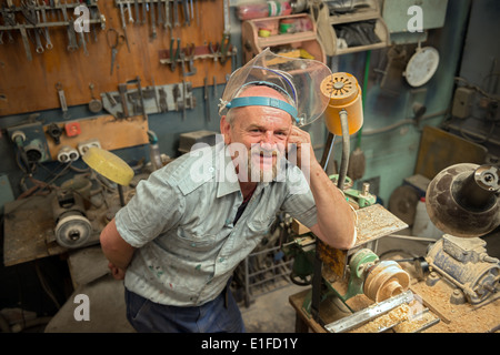 Il vecchio uomo appoggiò il gomito sul legno tornio in officina di casa. Foto Stock