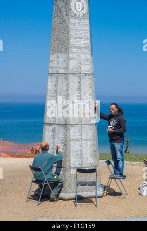 La spiaggia di Omaha, in Normandia, Francia. Lavoratori re-paint i nomi dei caduti sul memoriale della prima divisione di fanteria. Foto Stock