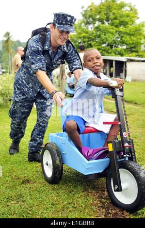 Stati Uniti Navy musicista di terza classe Smilen Travis, sinistra, spinge un Vanuatuan bambino su un triciclo a Espiritu Santo, Vanuatu, 6 Maggio 201 Foto Stock