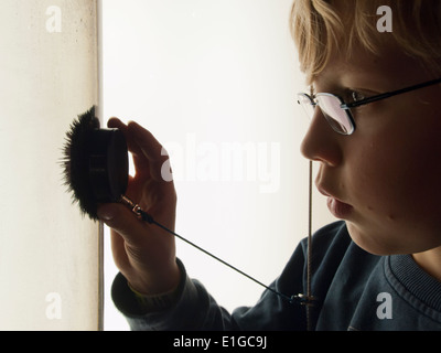Un 12-anno vecchio ragazzo sta guardando la limatura di ferro in un serbatoio di acqua che sono attratti da un magnete forte tenuta in mano al fanciullo Foto Stock