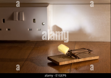 In vecchio stile in legno mousetrap accanita con formaggio giallo crumb pronto per la cattura di un mouse su pavimento in rovere vicino alla presa elettrica Foto Stock