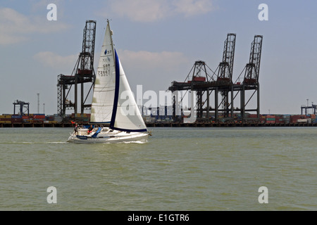 Imbarcazione a vela in viaggio passato gru a Felixstowe docks, Suffolk, Regno Unito Foto Stock