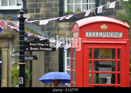 Telefono rosso scatola cartello turistico e un turista giapponese sotto la pioggia a Haworth, West Yorkshire Foto Stock