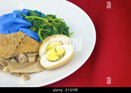 Close up blu a base di noodle di riso con tofu fritto, spinaci, abalone funghi e uovo bollito in salsa vegetariano su sfondo rosso. Foto Stock