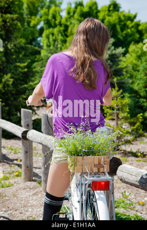 Vista posteriore del giovane ragazza in bici con cesto di fiori. Messa a fuoco selettiva Foto Stock