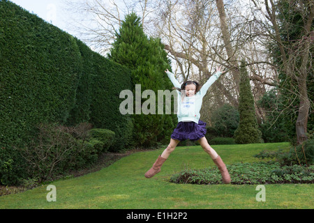 Ragazza giovane jumping metà aria in giardino Foto Stock