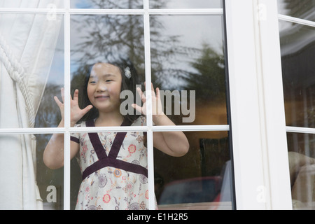 Ragazza giovane guardando fuori dalla stanza di seduta finestra Foto Stock