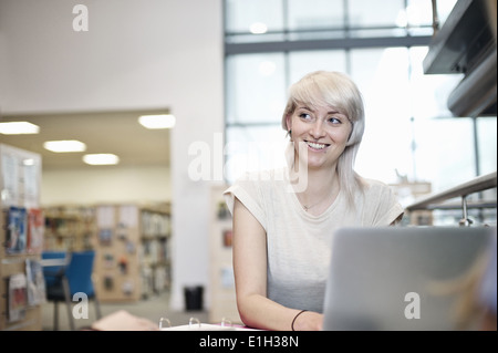 Giovane donna utilizzando laptop in biblioteca Foto Stock