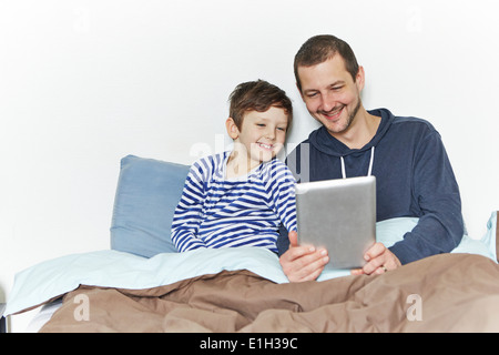 Padre e Figlio con tavoletta digitale a letto Foto Stock