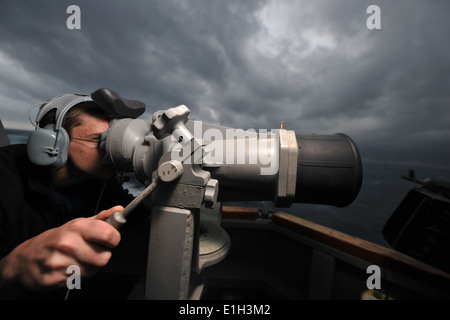 Stati Uniti Operazioni navali specialista marinaio Anthony C. Tyrrell guarda attraverso la nave il binocolo sul ponte di ala a bordo della GUI Foto Stock