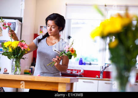 Giovane donna disponendo dei fiori in cucina Foto Stock