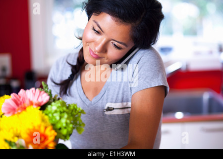 Giovane donna utilizzando un telefono cellulare in cucina Foto Stock