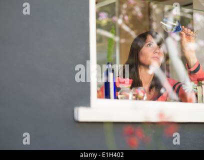 Donna matura a casa esaminando la finestra vetro del vino Foto Stock