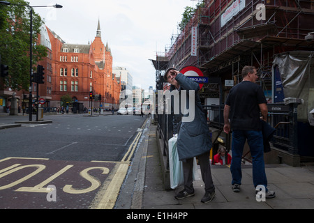 Un uomo anziano ripara i suoi occhi come lui guarda giù per la strada per un bus sul trefolo a Londra. Foto Stock