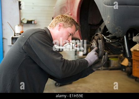 Un meccanico in un garage è controllare e riparare i freni di un auto sollevata. Foto Stock