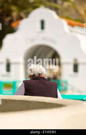 Capelli grigi donna si siede sul lungomare sulla Via Casino modo leggendo un libro. Avalon, Isola Catalina, California. Foto Stock