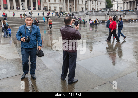 I turisti scattare fotografie in un umido Trafalgar Square, Londra. Foto Stock