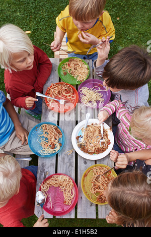 Vista aerea di sette bambini mangiare spaghetti al tavolo da picnic Foto Stock