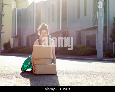 Giovane donna accovacciata per sollevare la pila di scatole di cartone Foto Stock