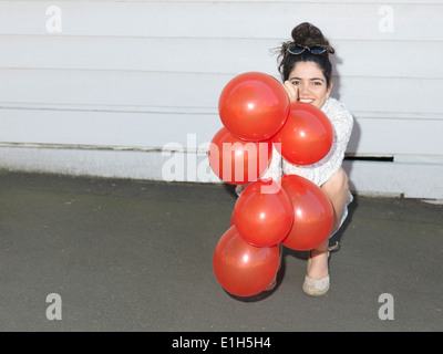 Ritratto di giovane donna accovacciata con un mucchio di palloncini Foto Stock
